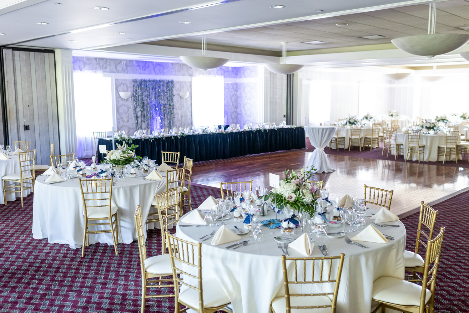 View of the dining area for a wedding reception. Each table is decorated with white tableware.