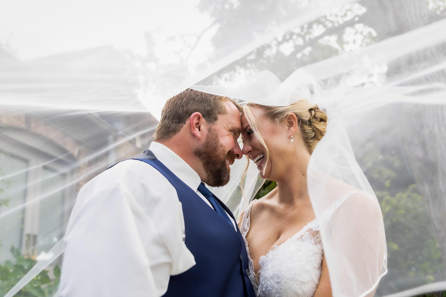 A loving couple on their wedding day, smiling while facing each other and foreheads touching.