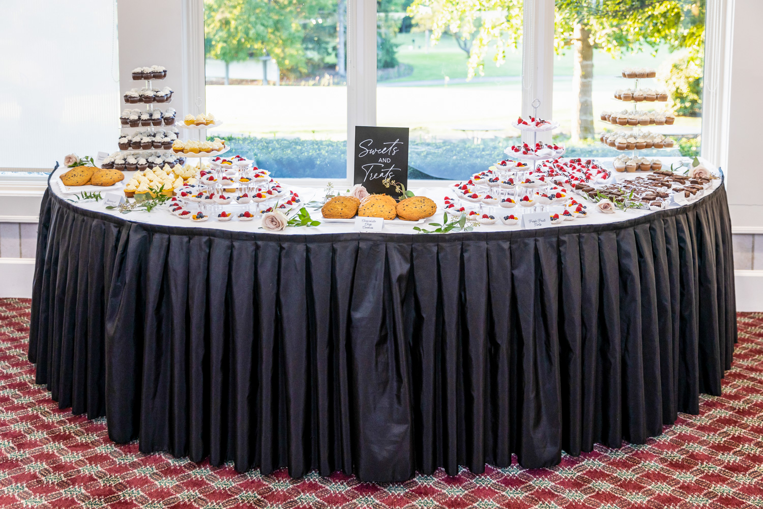 The deserts table at a wedding. Various cakes and other treats are neatly laid out.